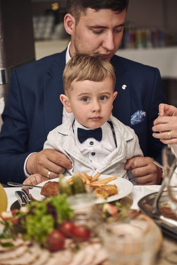 Uroczy chłopiec siedzący u taty na kolanach przy stole - reportaż