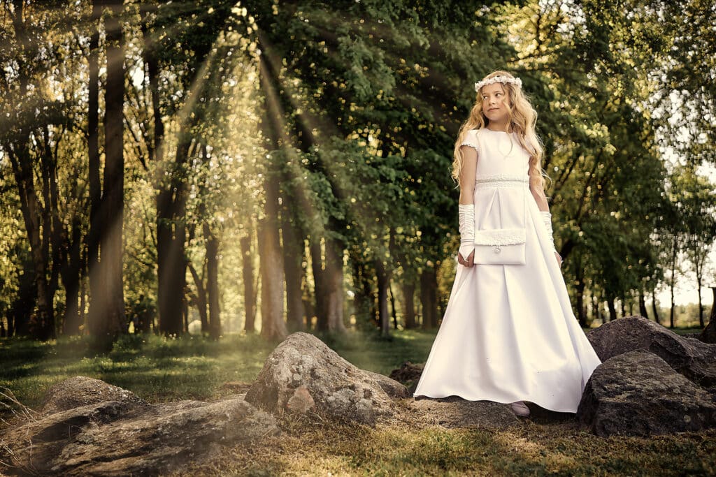 Sesja komunijna - dziewczynka pozuje wśród kamieni i promieni słońca
