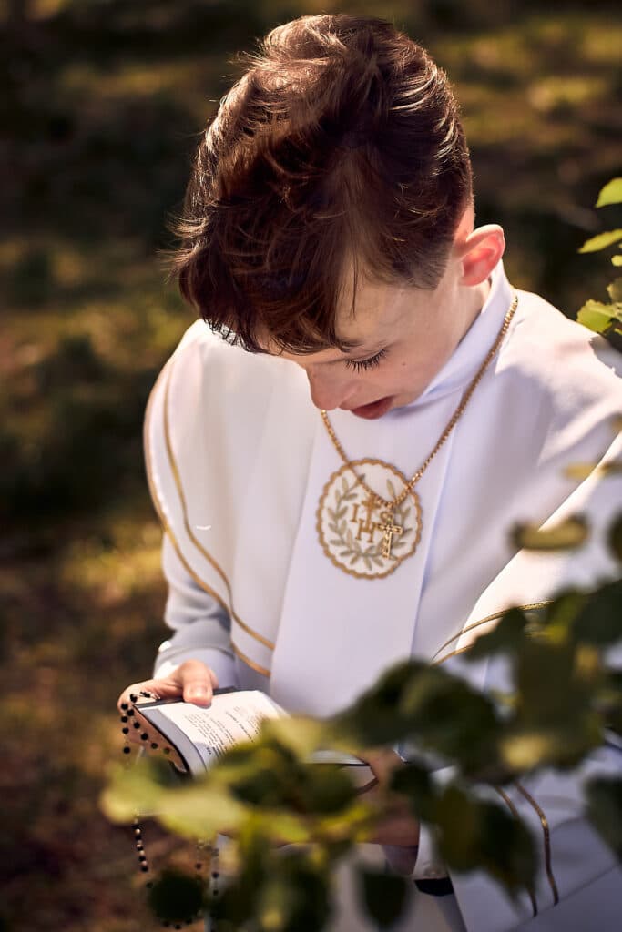 Sesja Komunijna - chłopie modli się z książeczką.