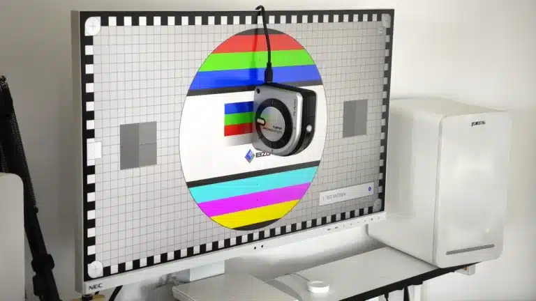 Kalibracja monitora - Monitor NEC z białymi ramkami wyświetla planszę testową EIZO, używaną do kalibracji monitorów i oceny jakości obrazu. Na środku ekranu, w okręgu z pasami kolorów, wisi kalibrator Calibrite ColorChecker Studio, aktywnie mierzący parametry wyświetlacza. Tło planszy stanowi siatka i skala szarości, co jest kluczowe dla precyzyjnego zarządzania kolorem i zapewnienia dokładnego odwzorowania barw.