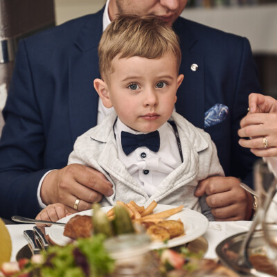 Uroczy chłopiec siedzący u taty na kolanach przy stole - reportaż