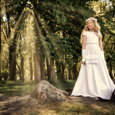 Sesja komunijna - dziewczynka pozuje wśród kamieni i promieni słońca