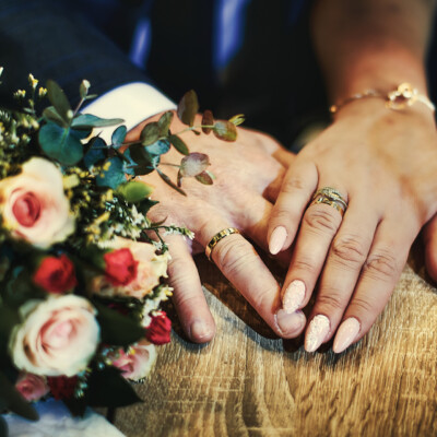 Splecione ręce pary Młodej z obrączkami i bukietem